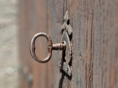 An antique iron key in the lock of a weathered wooden door.