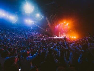 Arena crowd at a night event under blue and orange stage lights, seen from the stands