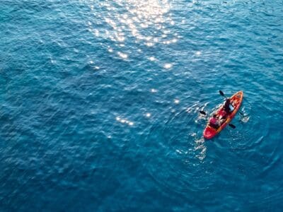 A red kayak with two paddlers seen from above on deep blue water